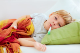 Crianças com febre deitada na cama com um termômetro na boca.