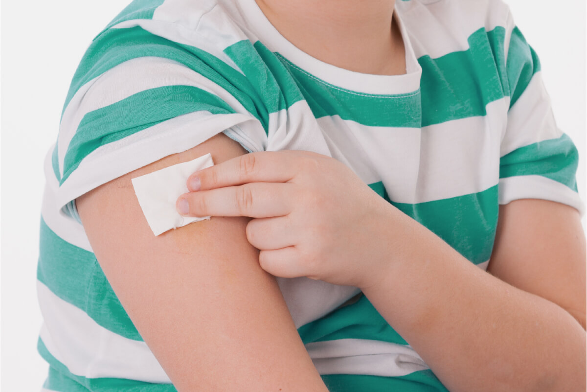 Menino segurando um curativo após tomar a vacina. Essa imagem ilustra o post dos 6 mitos sobre a vacinação. 