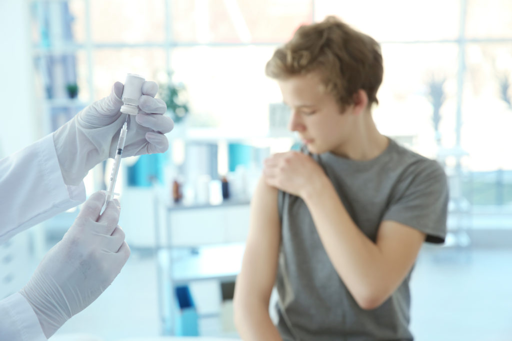 Menino olhando para o curativo da vacina para adolescentes