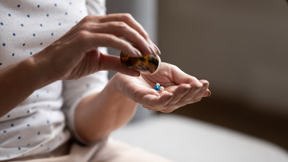 Mulher com um frasco de medicação na mão colocando algumas pílulas de remédios na outra. Essa imagem é para ilustrar que tomar remédios por conta própria pode causar alergia a medicamentos.