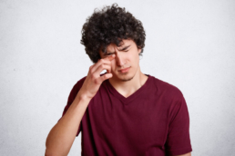 Homem coçando os olhos, um dos sintomas mais frequentes de conjuntivite alérgica.