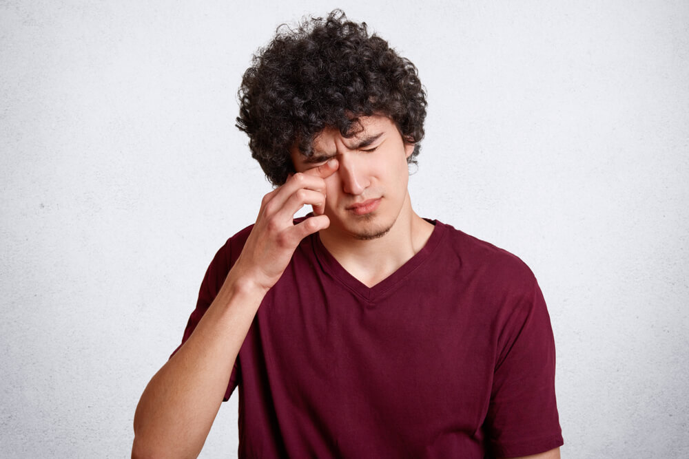 Homem coçando os olhos, um dos sintomas mais frequentes de conjuntivite alérgica.