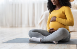 Mulher com blusa amarela sentada no chão fazendo carinho na barriga. A imagem representa o post sobre qual exame de sangue detecta gravidez.