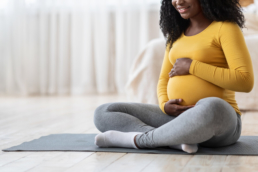 Mulher com blusa amarela sentada no chão fazendo carinho na barriga. A imagem representa o post sobre qual exame de sangue detecta gravidez.