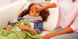 Mãe medindo a temperatura da filha resfriada. A imagem ilustra o post sobre a diferença entre gripe e resfriado.