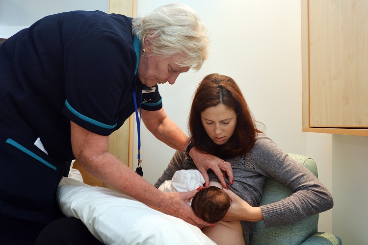 A imagem mostra uma consultora de amamentação orientando uma mãe que está com um bebê em seu colo