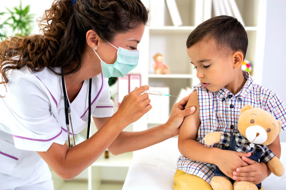 uma mulher profissional da saúde aplicando vacina no braço de um menino - vacina coqueluche