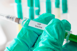 uma mão com luva verde segurando uma seringa com a descrição de vacina vip