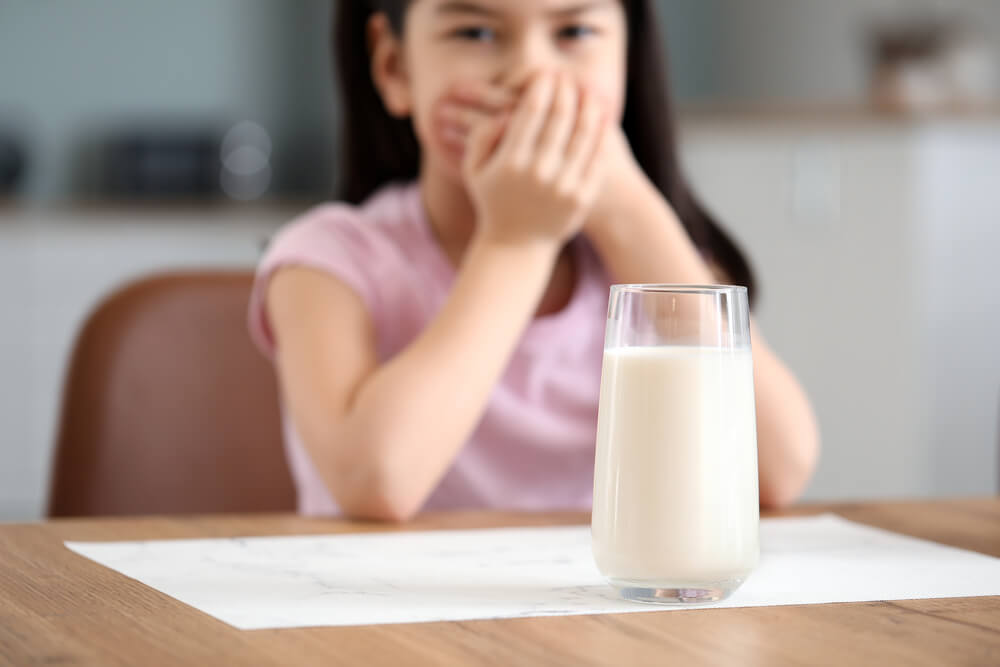 imagem mostrando uma menina tampando a boca de frente pra um copo de leite - alergia à proteína do leite
