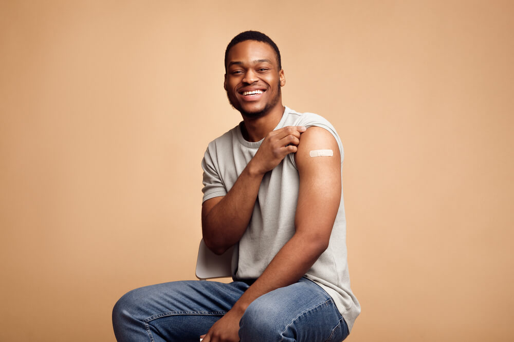 Homem afrodescendente mostra o braço com o curativo depois de ter se protegido contra uma das doenças preveníveis por vacinas
