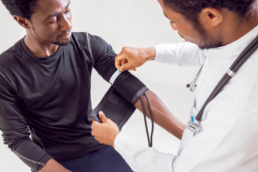 Imagem mostra um médico medindo a pressão do paciente antes de prescrever exames masculinos para a pessoa.