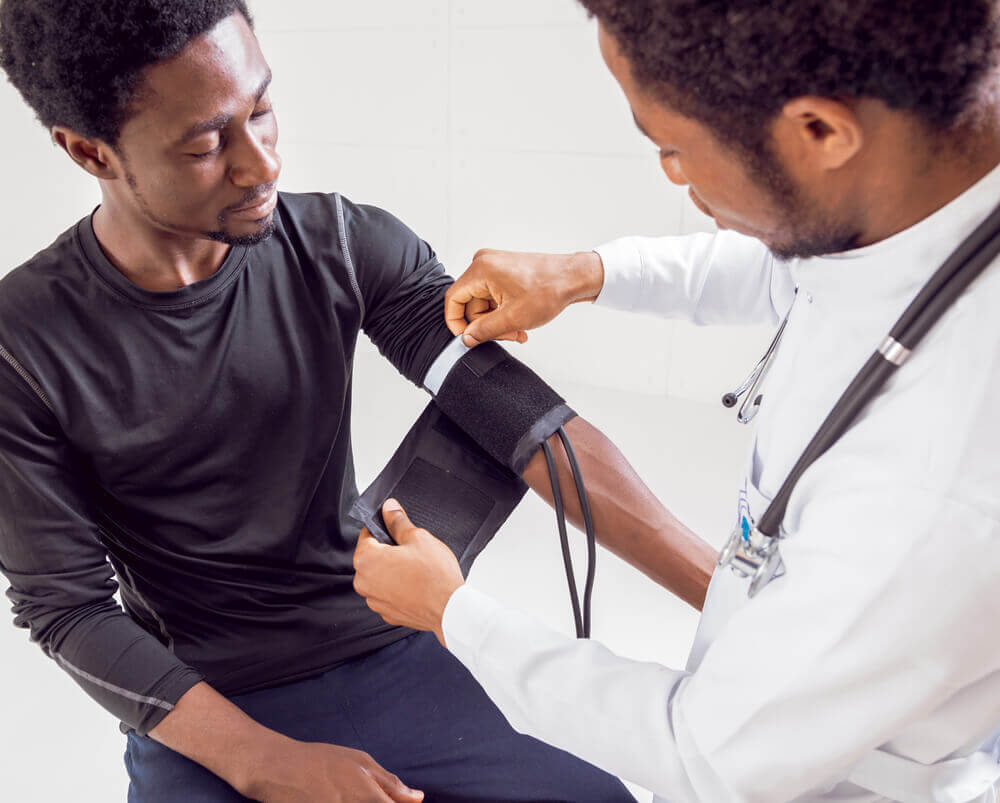 Imagem mostra um médico medindo a pressão do paciente antes de prescrever exames masculinos para a pessoa.