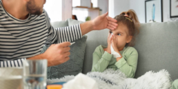 Homem coloca a mão na testa de uma menina gripada para medir a temperatura dela, um dos sintomas da gripe