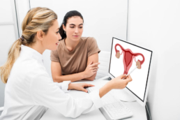 Médica mostra uma ilustração do aparelho reprodutor feminino na tela do computador para a paciente. Essa imagem ilustra o post sobre o câncer de colo de útero.