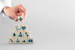 Pilha de cubinhos. Cada um tem um símbolo na frente que representa algo relacionado à saúde. No topo, uma mão coloca o último cubinho. Essa imagem ilustra o post sobre o Dia Mundial da Saúde.