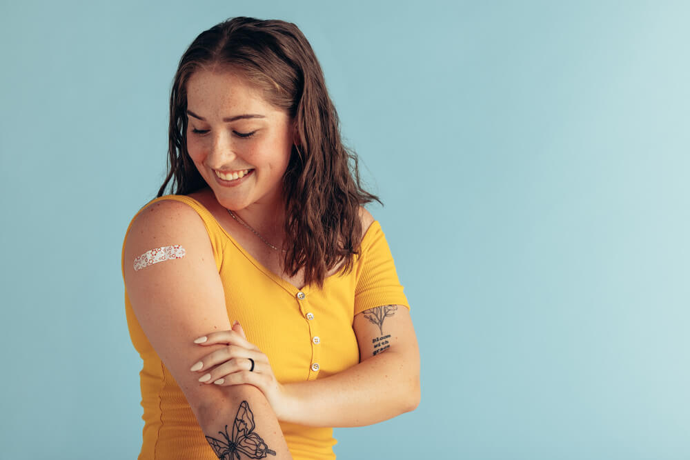 Menina feliz olha para o adesivo colocado no braço após a aplicação da injeção. Essa imagem ilustra a capa do post sobre quais são as doenças imunopreveníveis