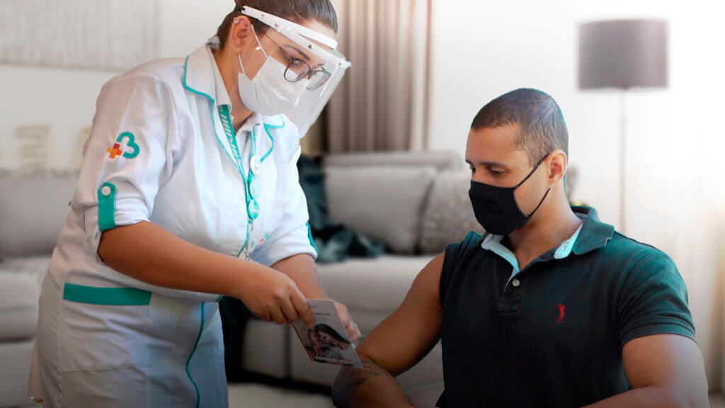 Enfermeira da Beep prepara o material para vacinar um homem sentado na cadeira e com máscara. Essa imagem representa o post sobre vacina gripe para empresas.