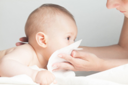 Bebê assoando o nariz em um papel segurado pela mãe, esses sintomas são característicos da infecção pelo vírus sincicial respiratório (VSR)