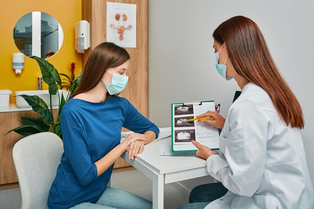 mulher grávida olhando para o exame pré-natal que está na mão da ginecologista.