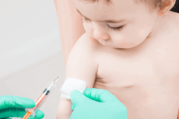 Bebê olhando para a seringa da vacina meningocócica ACWY.