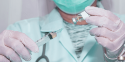 Técnica de enfermagem usando máscara facial segura uma ampola de vacina pneumocócica 13 e passa o líquido para a injeção.
