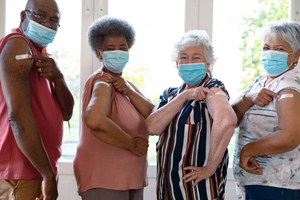 imagem mostra quatro idosos apontando para o adesivo que colocam após a aplicação da vacina, de acordo com a tabela de vacinas por idade