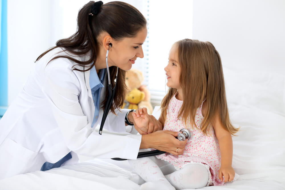 Imagem mostra uma pediatra examinando uma criança que esta sentada