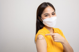 Imagem mostra uma mulher apontando para o adesivo colocado após ela tomar a vacina da gripe