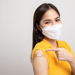 Imagem mostra uma mulher apontando para o adesivo colocado após ela tomar a vacina da gripe