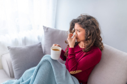 Mulher sentada no sofá com um café na mão tentando alternativas sobre como desentupir o nariz