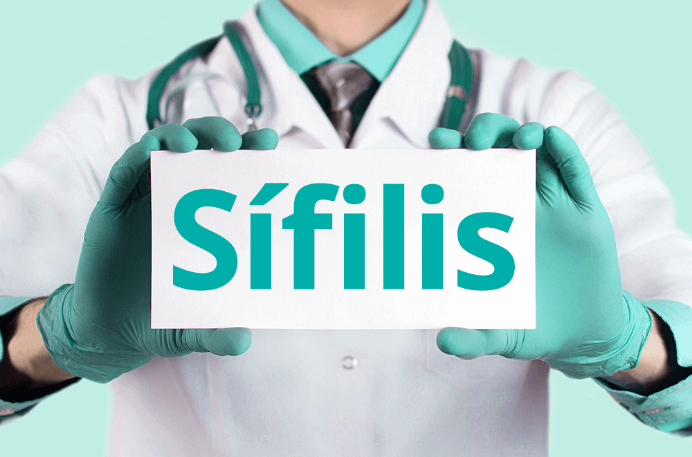 Imagem mostra um médico ao fundo com uma das mãos para frente segurando um cartão branco escrito sífilis