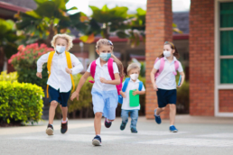 A imagem mostra 4 crianças usando máscara e correndo na escola