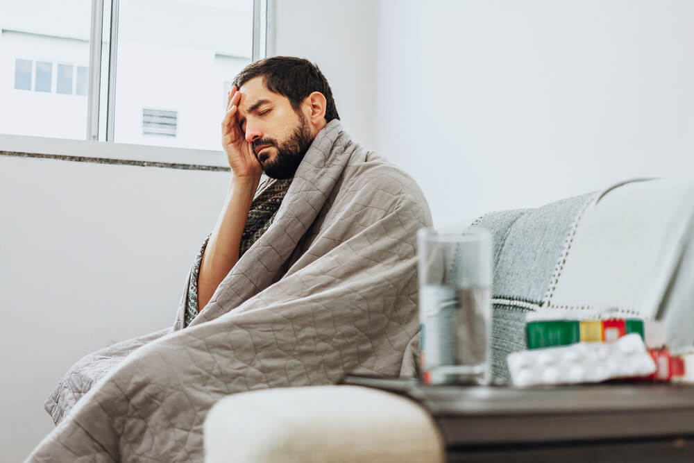 Homem enrolado no cobertor apresentando sintomas de infecção causada pelo vírus Influenza
