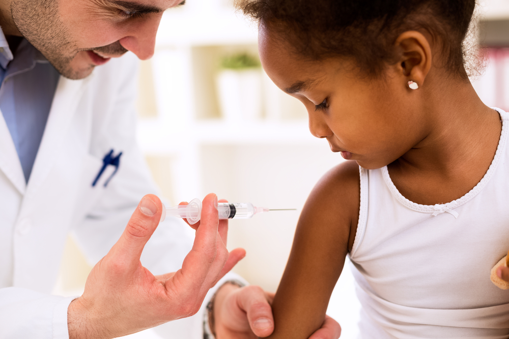 imagem mostra um médico aplicando uma vacina em uma menina